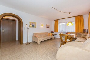 Ein Wohnzimmer mit einer Couch, einem Esstisch mit Stühlen, einer Stehlampe und einem Fenster mit Vorhängen.