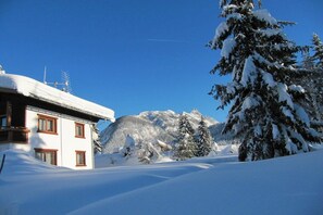 A snow-covered mountain landscape with a building featuring a balcony and a snow-covered tree. - Romantic mountain accommodation on the 1st floor (Leutasch)