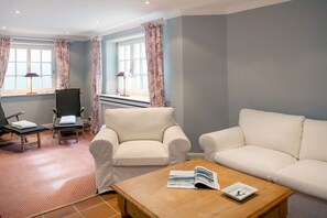 Een kamer met een bank, fauteuil, massagetafel en een raam met gordijnen.