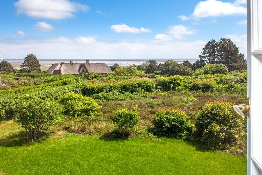 Et kystlandskab med et hus med stråtækte tage, frodig vegetation og havudsigt.