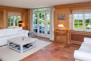A cozy room with a white sofa, a coffee table with books, a lamp, and a view through large windows. - Wiesenhof with a view of the Wadden Sea (Kampen)