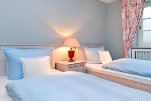 Ein Schlafzimmer mit zwei Betten, einem Nachttisch mit Lampe und einem Fenster mit Vorhängen.