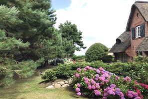 A traditional house with a thatched roof, surrounded by a well-maintained garden with various shrubs and trees. - Wiesenhof with a view of the Wadden Sea (Kampen)