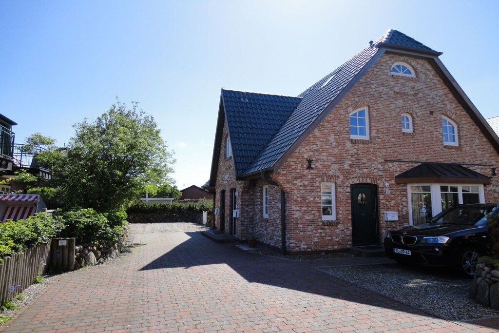 A brick building with a sloped roof, a black car parked in front, and a paved driveway.