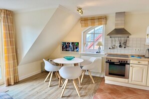 Une cuisine avec des meubles blancs, un fourneau et une fenêtre donnant sur un bâtiment à l’extérieur.
