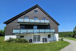 A two-story building with a balcony on the upper floor, a garage door, and a paved driveway. - Holiday apartment with 2 bedrooms (Altenberg)