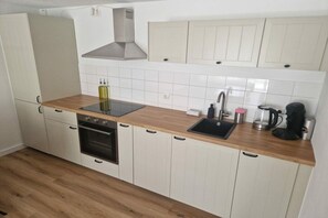 A compact kitchen with white cabinets, a wooden countertop, a built-in oven, a stainless steel sink, and a coffee maker. - Holiday apartment with 2 bedrooms (Altenberg)