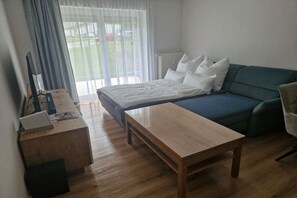 Een kamer met een bed, een slaapbank, een houten tafel en een bureau met een computer en boeken.