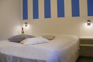 A hotel room with a bed, pillows, a nightstand, and wall-mounted lights. - Holiday apartment with 1 bedroom (Breege\/Juliusruh OT Juliusruh)