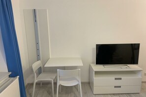 A room with a white desk, a white chair, a television on a stand, and a blue curtain. - Holiday apartment with 1 bedroom (Breege\/Juliusruh OT Juliusruh)