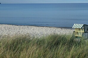 Une plage avec une chaise de plage à rayures et de l’herbe au premier plan.