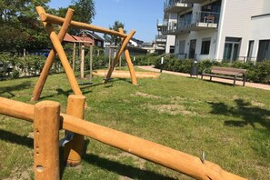 A playground with wooden structures, a bench, and a building in the background. - Holiday apartment in Glowe with swimming pool (Glowe)