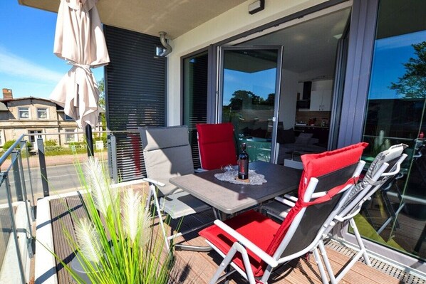 Ein Balkon mit Tisch und Stühlen, eine Schiebetür zu einem Wohnbereich und Blick auf die Straße.
