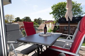 Ein Balkon mit Tisch, Stühlen, einer Flasche und einem roten Kissen.
