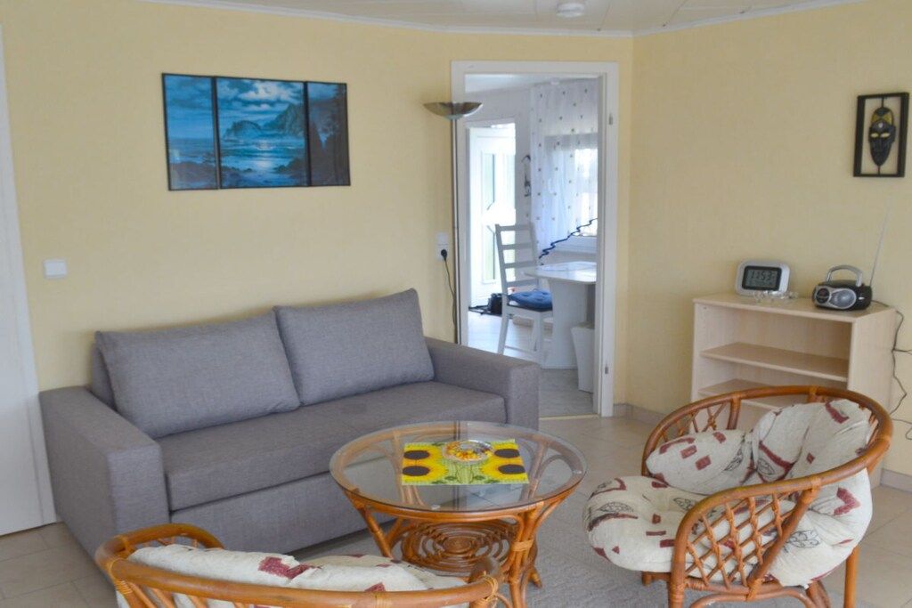Ein Wohnzimmer mit einer Couch, einem Glastisch, Korbstühlen und einem Radio.