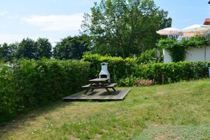 A backyard with a wooden picnic table, a white birdhouse, and a white wall with climbing plants. - Holiday home with 2 bedrooms (Plau am See)