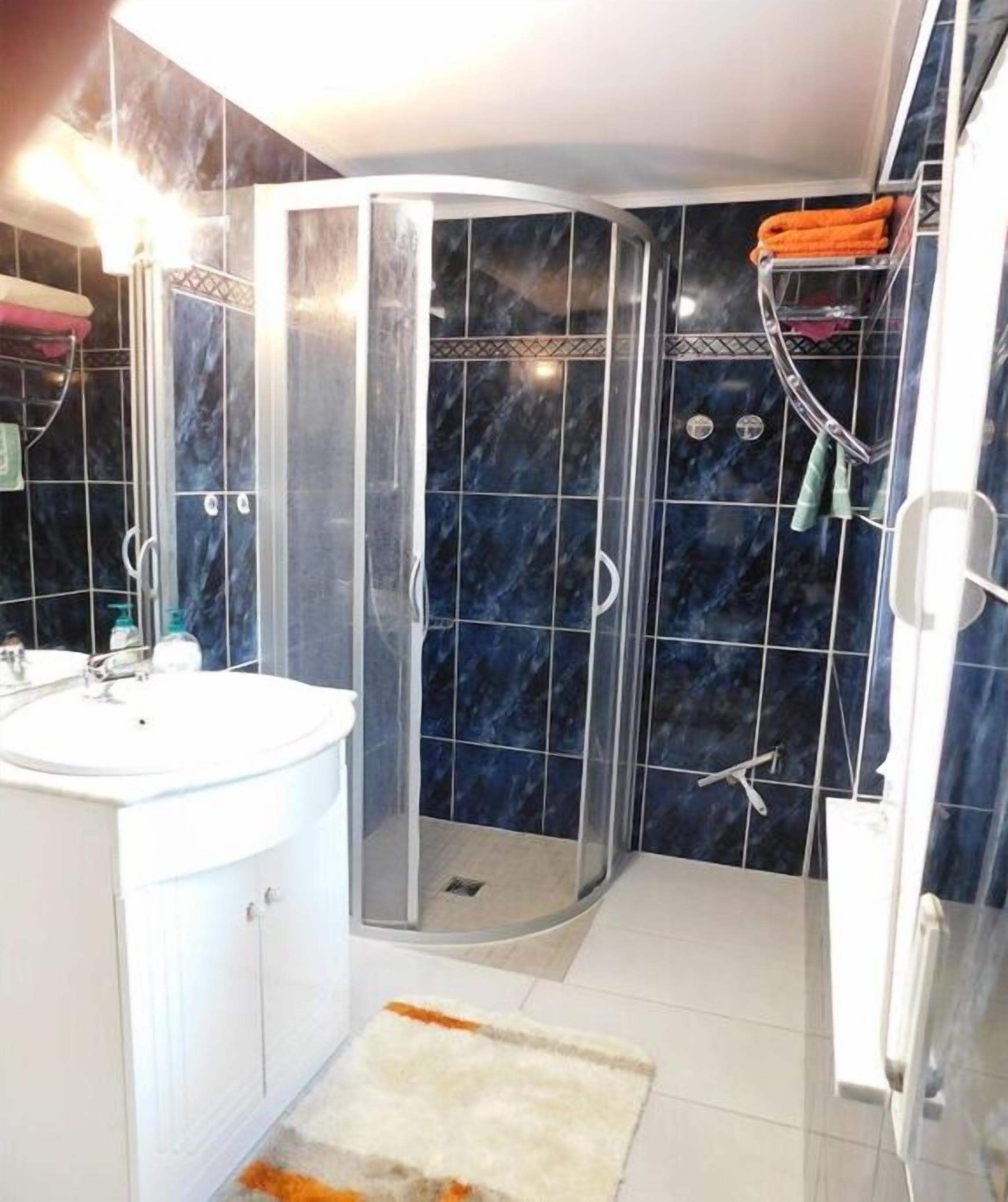 Ein Badezimmer mit einer gläsernen Dusche, einem weißen Waschbecken und einem Fliesenboden.