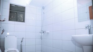 Un baño con paredes de azulejos blancos, un inodoro, una ducha con cabezal de ducha manual y un lavamanos.