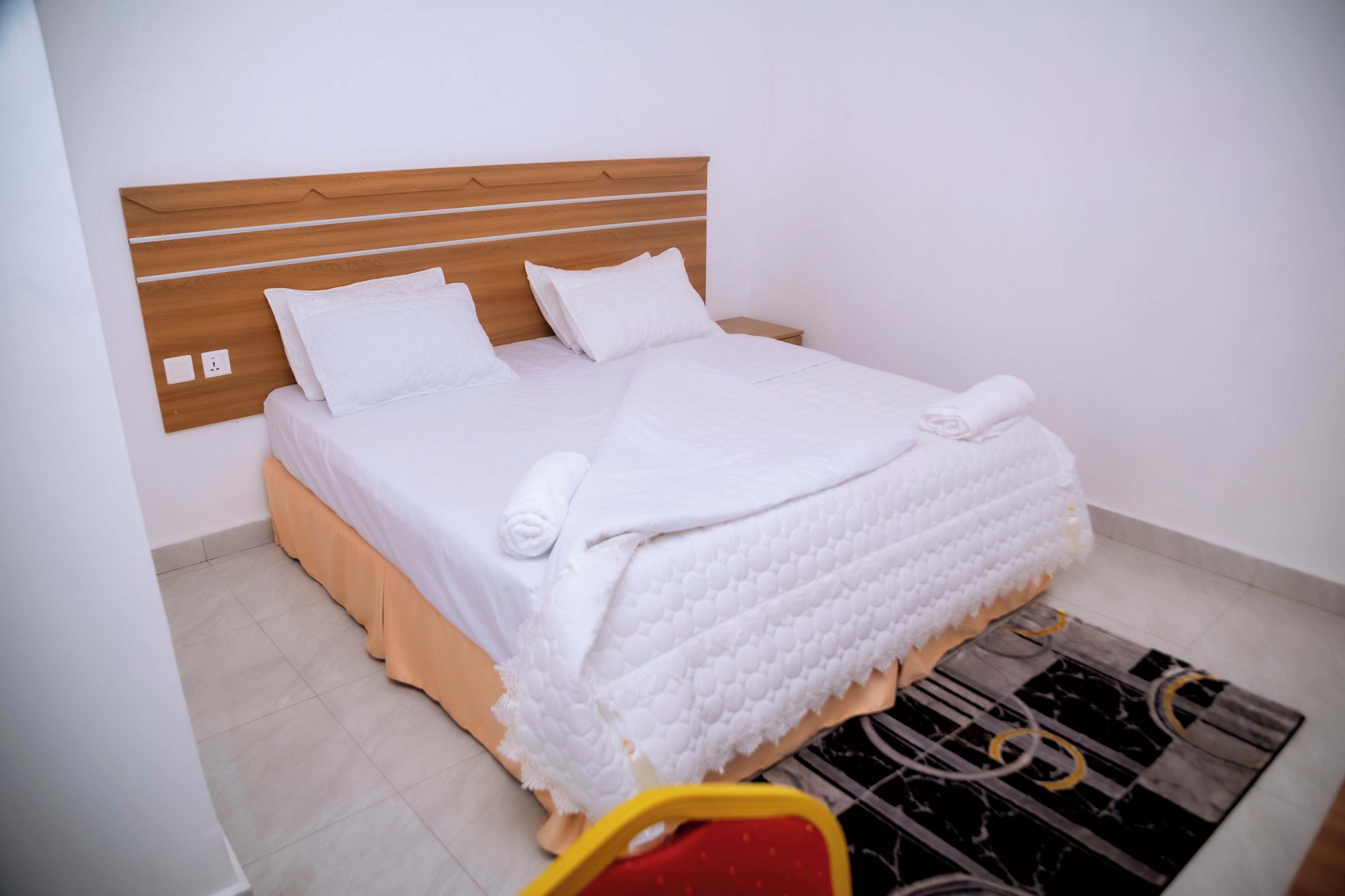 Una cama bien hecha con ropa de cama y almohadas blancas, un cabecero de madera y una mesita de noche con una toalla.