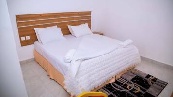Una cama bien hecha con ropa de cama y almohadas blancas, un cabecero de madera y una mesita de noche con una toalla.