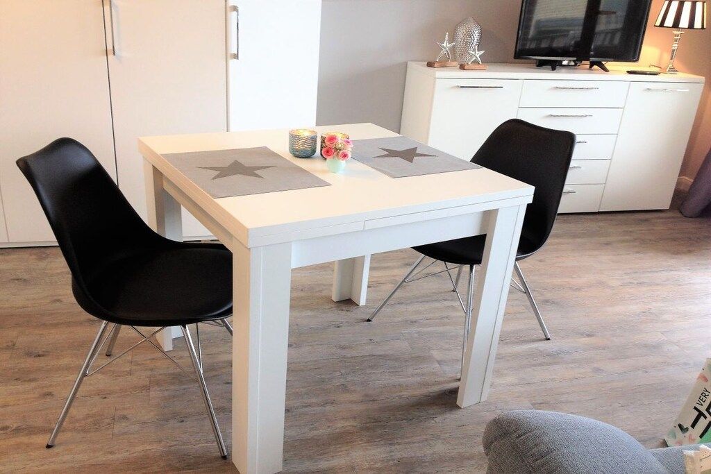 Een eethoek met een witte tafel, twee zwarte stoelen en een televisie op een wit kastje.