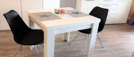 A dining area with a white table, two black chairs, and a TV on a white cabinet.