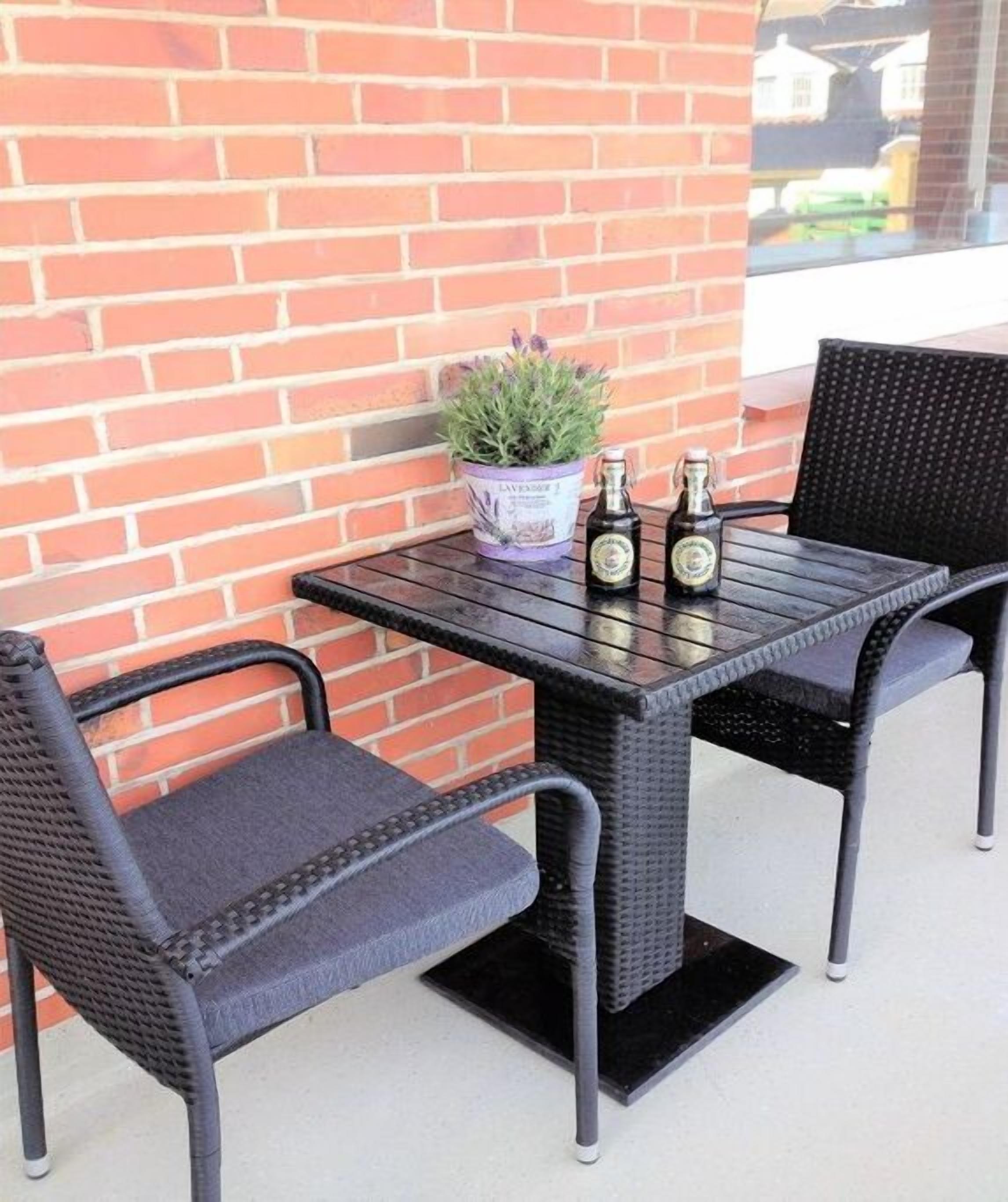 A patio table with two chairs, a potted plant, and two bottles.