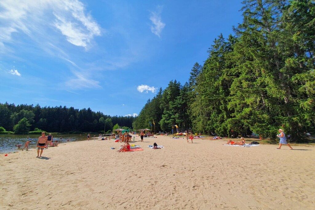 Uma praia com pessoas se banhando e tomando sol, rodeada por árvores e um céu claro.
