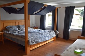 Quarto com cama de dossel, cabeceira de madeira e janela com cortinas.
