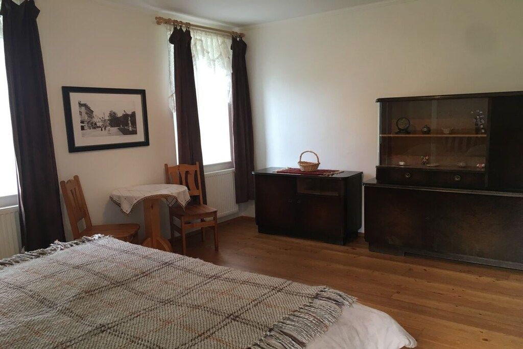 A room with a bed, a wooden desk, a chair, a table, a cabinet, and a framed picture on the wall.