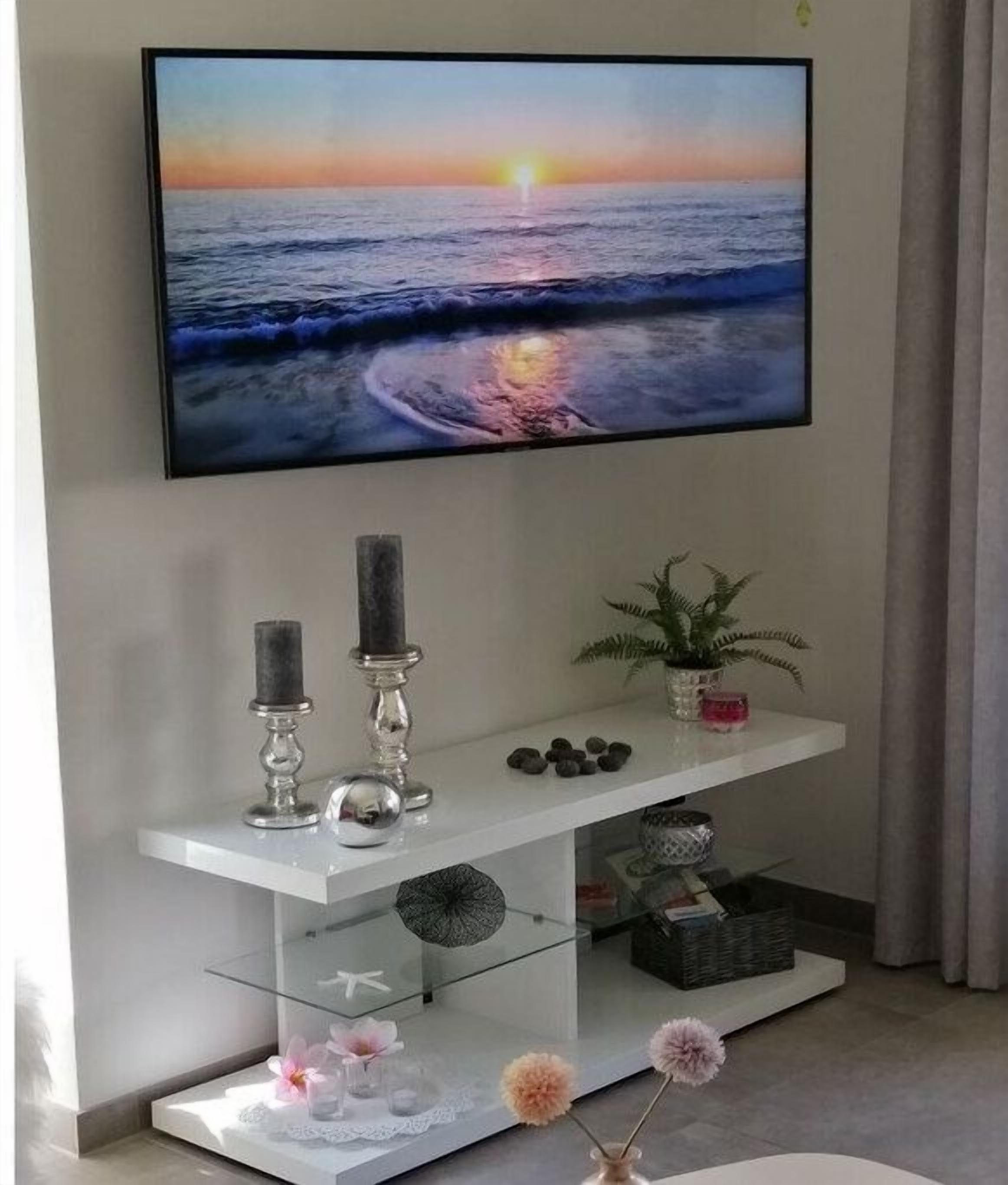 Un téléviseur à écran plat fixé au mur, une console blanche agrémentée d’objets décoratifs et une plante en pot.