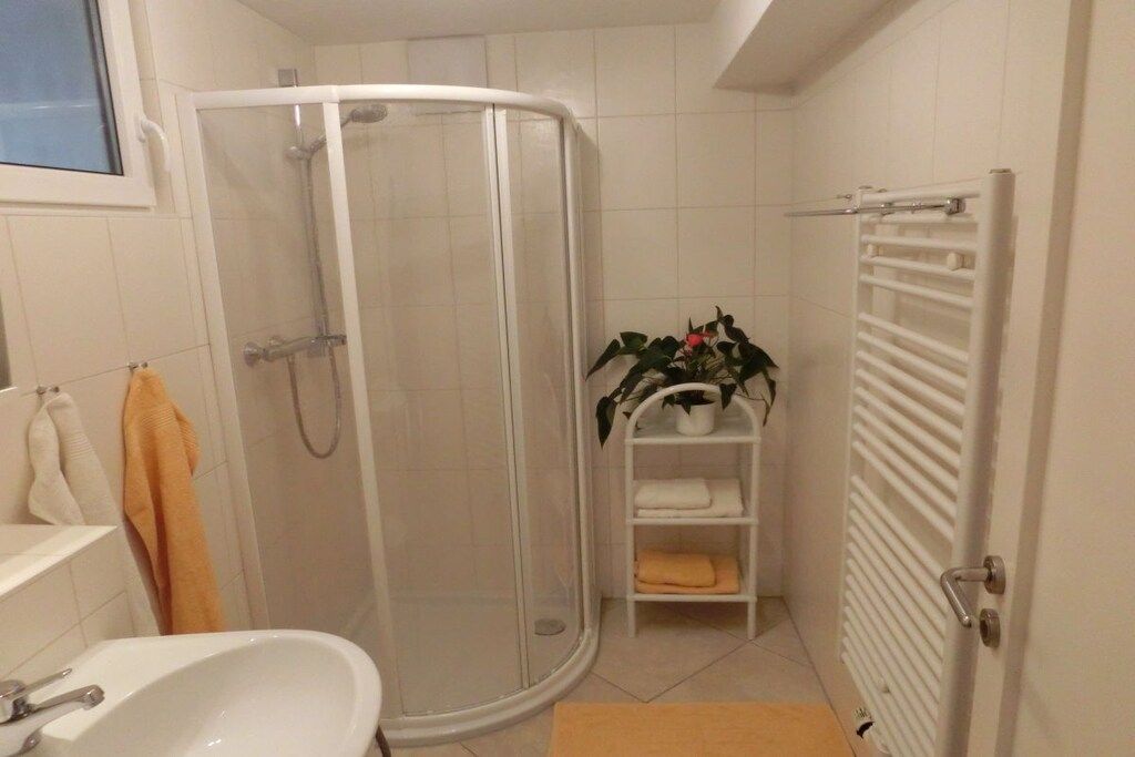 Une salle de bain équipée d’une douche, d’un lavabo, d’un porte-serviettes et d’une étagère où sont posés des serviettes et un pot de fleurs.