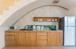 A kitchen with a stone backsplash, wooden cabinets, a microwave, a sink, and a refrigerator. - Kona Resort Pererenan E (Badung)