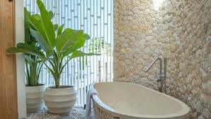 Une salle de bain avec une baignoire sur pieds, des murs en pierre et des plantes en pot.