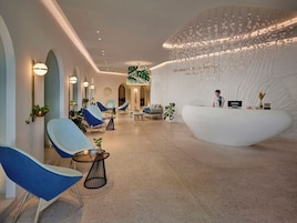 Un moderno área de recepción de spa con un mostrador curvo, zona de asientos con sillas y una pared grande con luces colgantes.