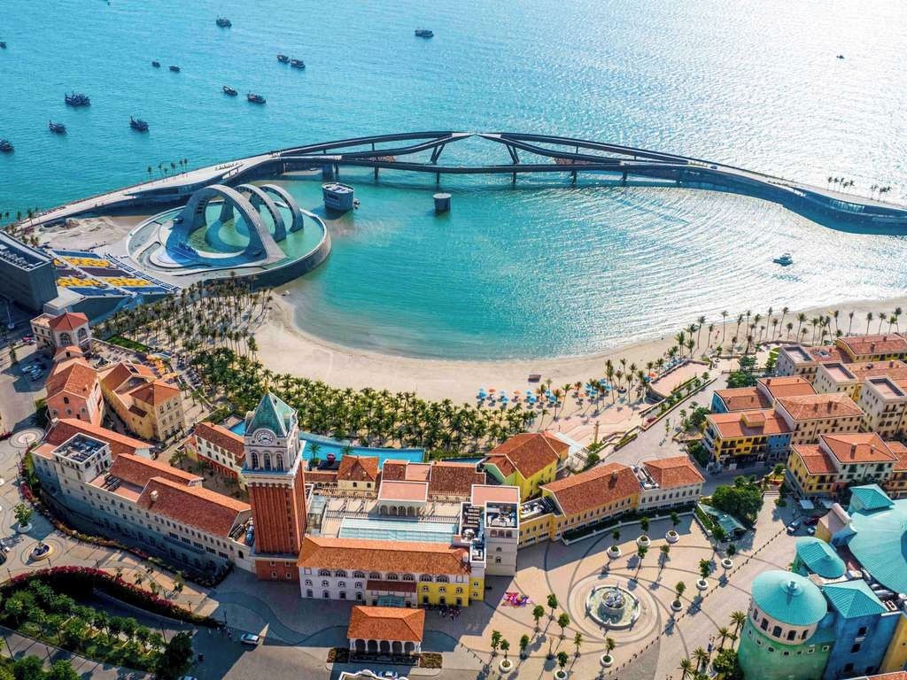Vista aérea de uma cidade costeira com uma igreja imponente, uma ponte e uma área de praia.