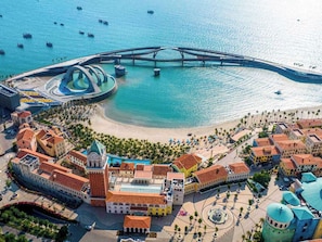 Vista aérea de un pueblo costero con una iglesia destacada, un puente y una zona de playa.