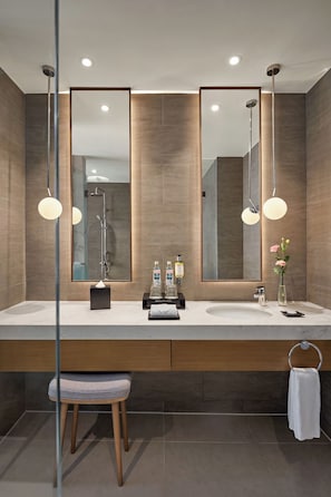 Un baño moderno con un espejo grande, dos lámparas colgantes, una ducha y un tocador con lavabo y toallero.