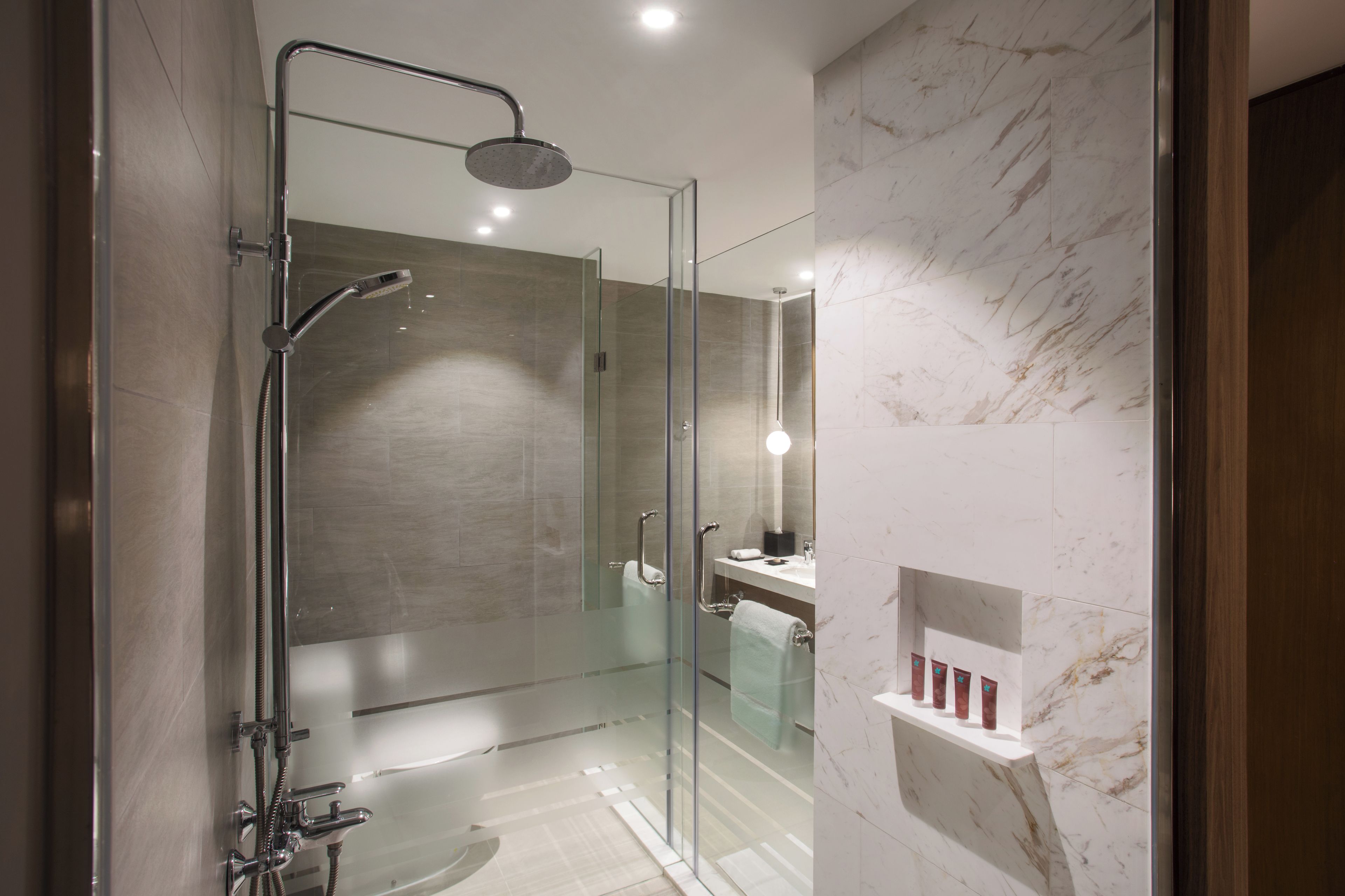 Un baño moderno con ducha acristalada, pared de azulejos de mármol y tocador con espejo.
