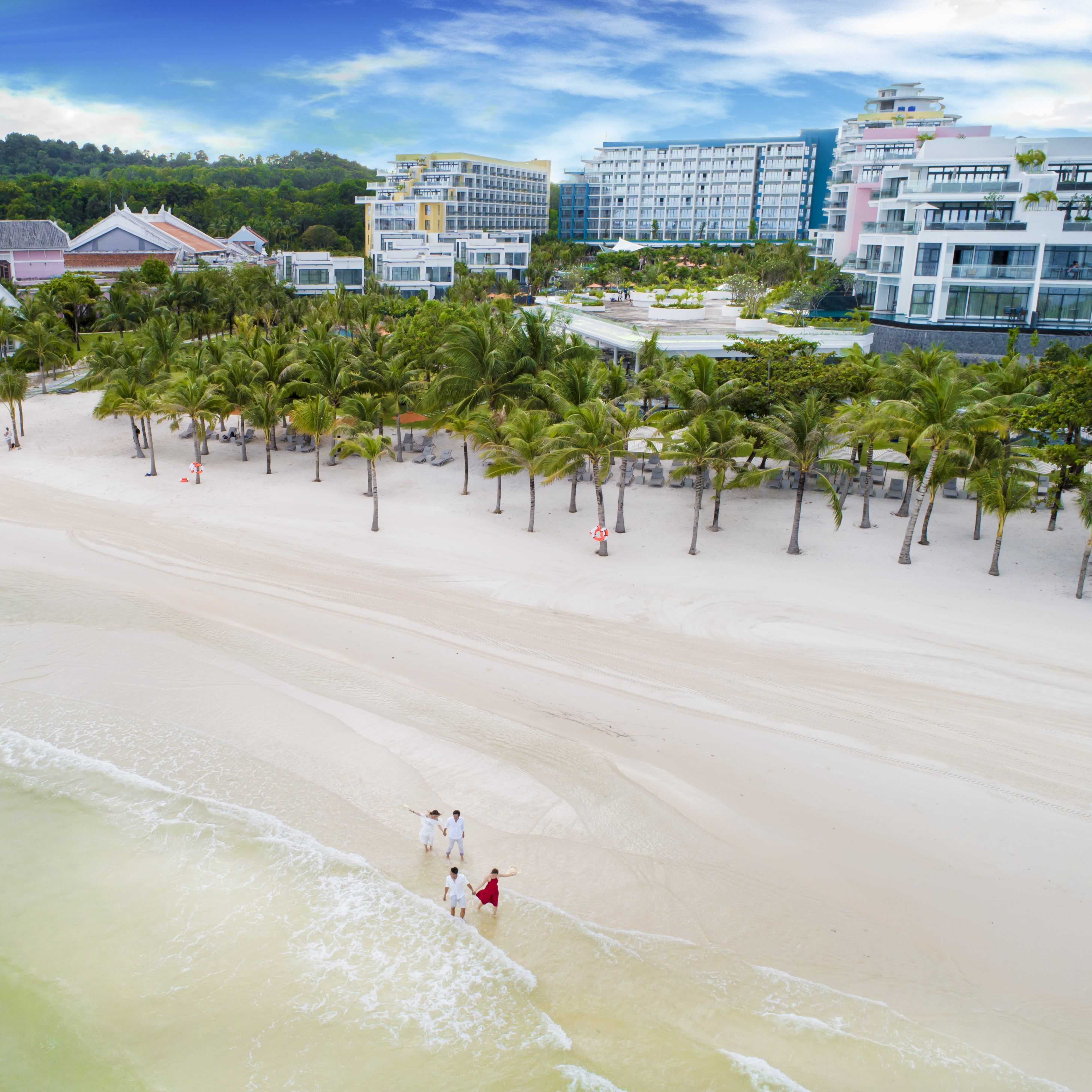 Una playa con palmeras y un complejo hotelero al fondo.