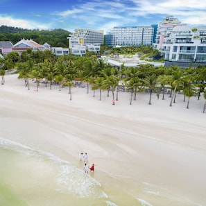 Una playa con palmeras y un complejo hotelero al fondo.