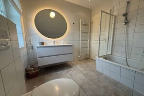 A modern bathroom with a round mirror, a bathtub, and a toilet. - Holiday home with 1 bedroom (Schönberg-Brasilien)