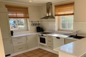 Una cocina con armarios blancos, estufa, lavamanos y una ventana con persianas.