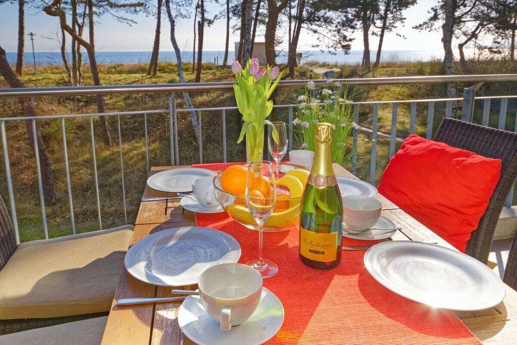 A table set for two with plates, cups, a bottle, and a vase of flowers, overlooking a natural landscape.