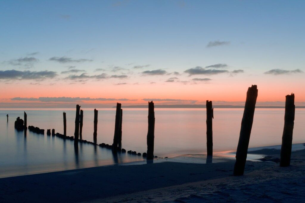 A beach with wooden posts and calm water.