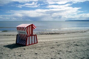 Een strand met een gestreepte strandstoel met de naam 'Seewind' en een rustige zee op de achtergrond.