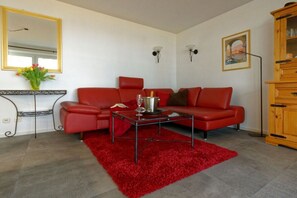 Een woonkamer met een rode bank, een bijzettafeltje, een rood vloerkleed, een kast en een wandspiegel.
