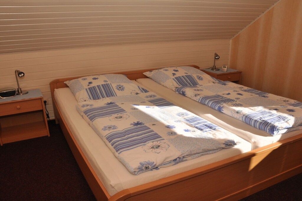 A twin bed with a floral bedspread, a bedside table with a lamp, and a window with blinds.