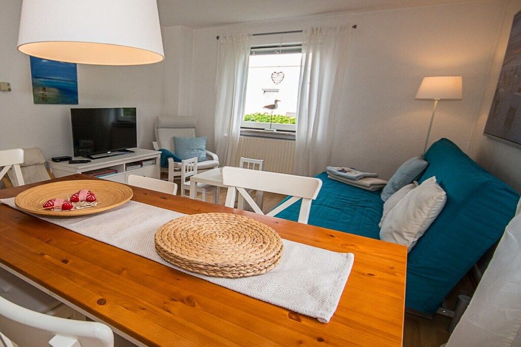 Une pièce chaleureuse avec une table à manger en bois, un téléviseur, un lit avec une literie bleue et une fenêtre avec des rideaux.