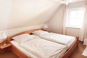 A single bed with a wooden frame and white bedding in a room with a sloped ceiling and a window with curtains. - Holiday home with 4 bedrooms (Timmendorfer Strand)